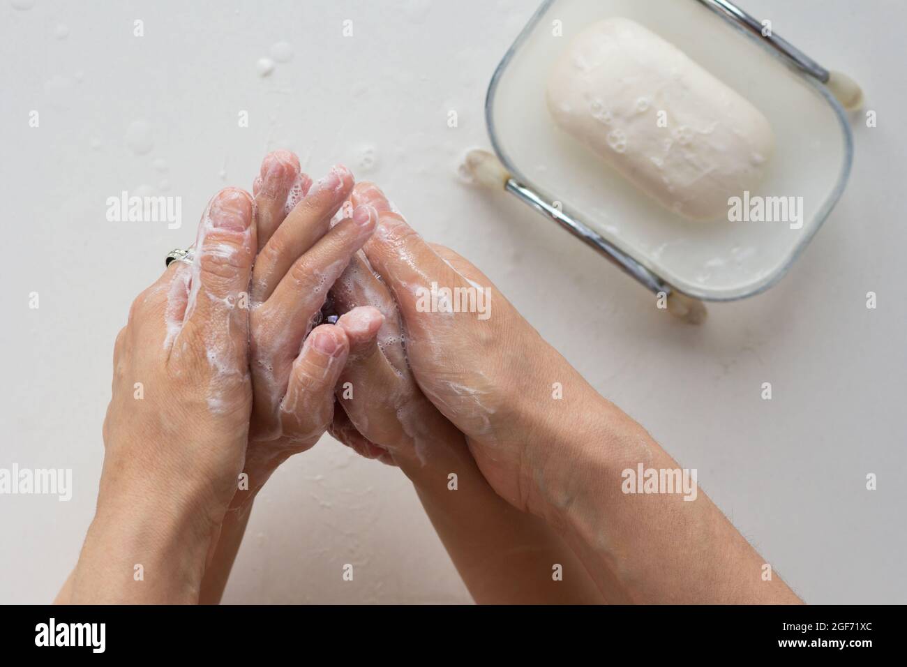 Vista dall'alto delle mani della donna che insaporite le mani del bambino con sapone su sfondo bianco Foto Stock