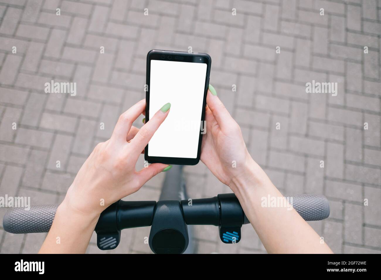 POV delle mani della donna che usa lo smartphone mentre si trova in piedi con uno scooter elettrico. Foto Stock