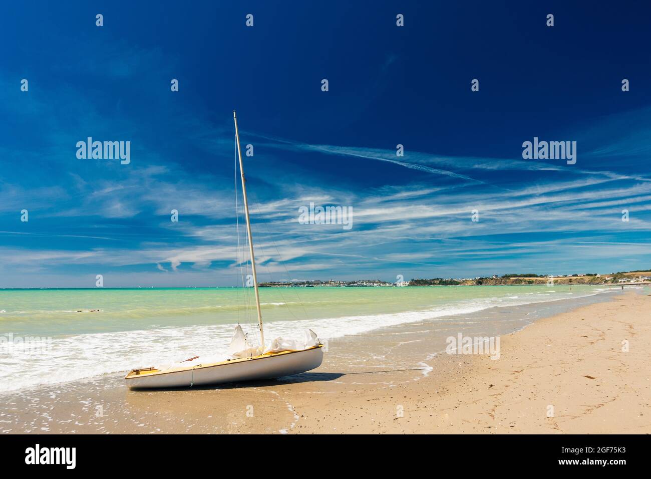 Grande spiaggia sabbiosa e barca a vela arenata su di essa con cielo blu e mare verde Foto Stock