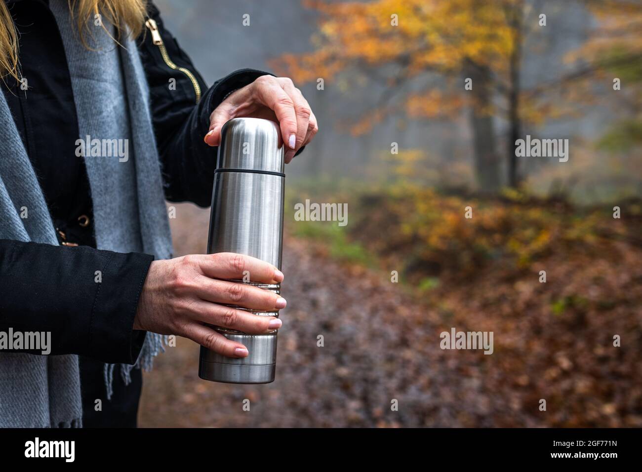 Donna che apre thermos con bevanda calda in autunno foresta durante l'escursione. Femmina turista che riposa in un terreno boscoso Foto Stock