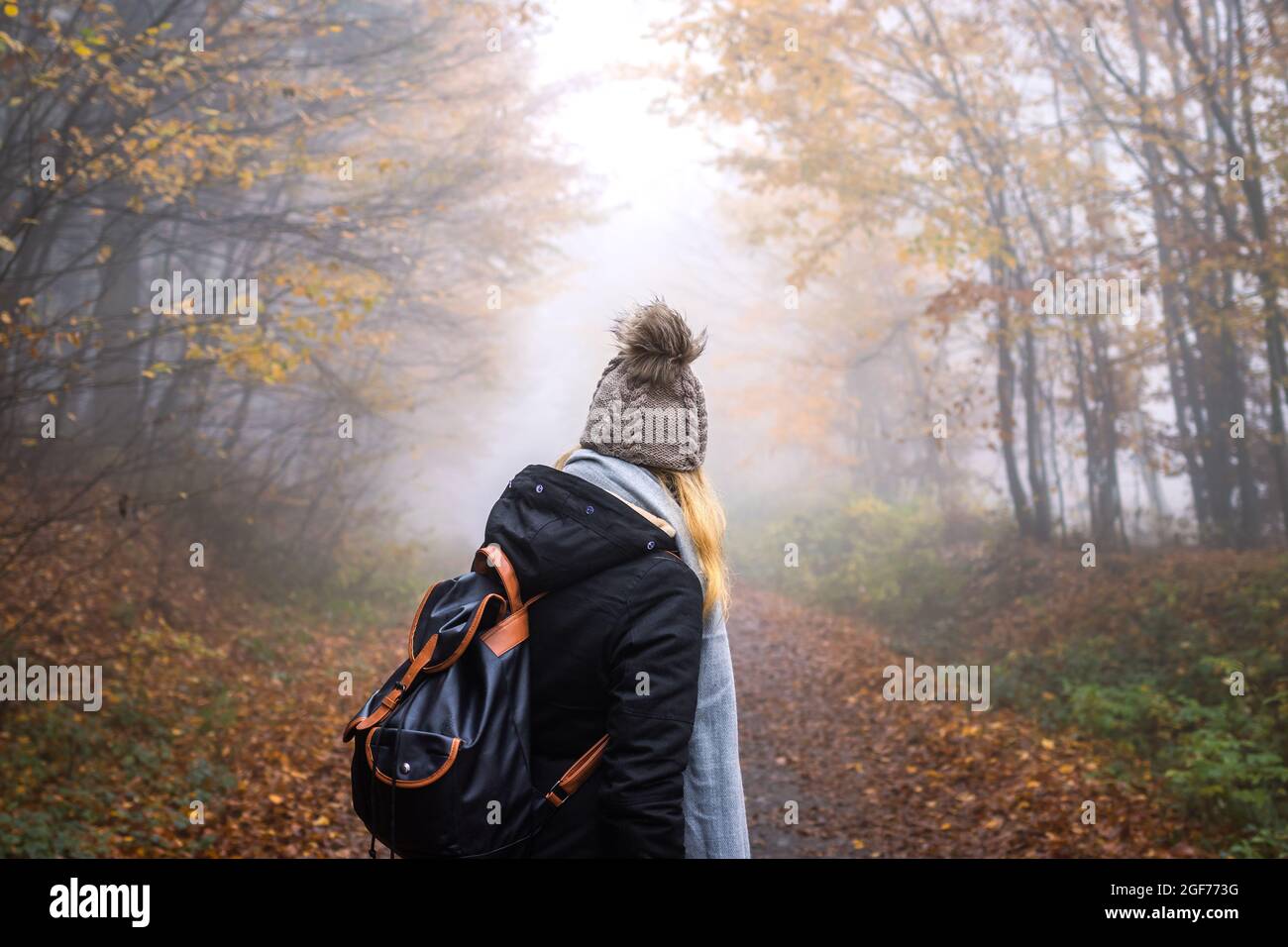 Donna con zaino e cappello a maglia escursioni nella foresta di nebbia. Turista alla ricerca di avventura nella natura Foto Stock