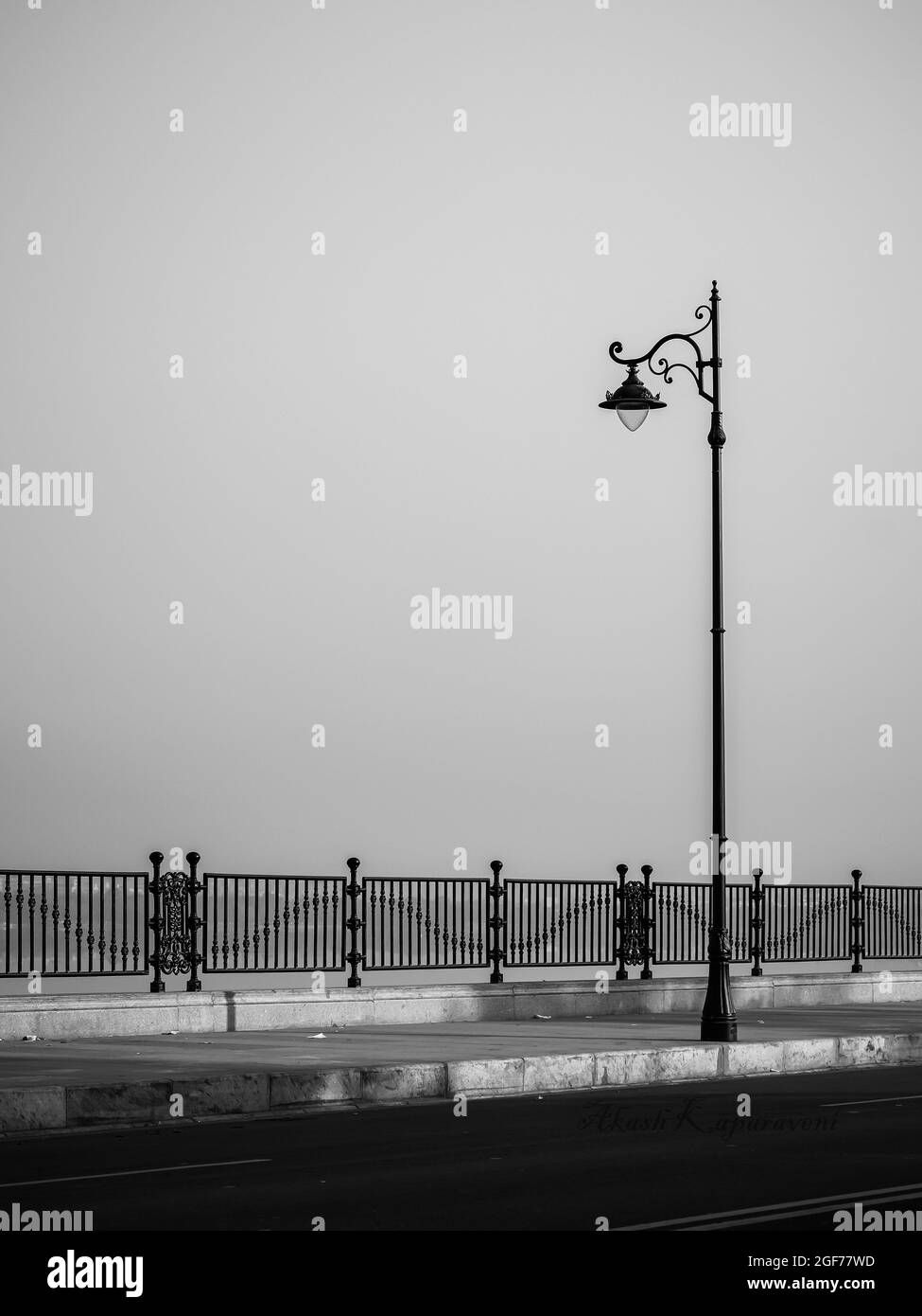 Scatto verticale di una luce stradale con marciapiede e recinzione Foto Stock