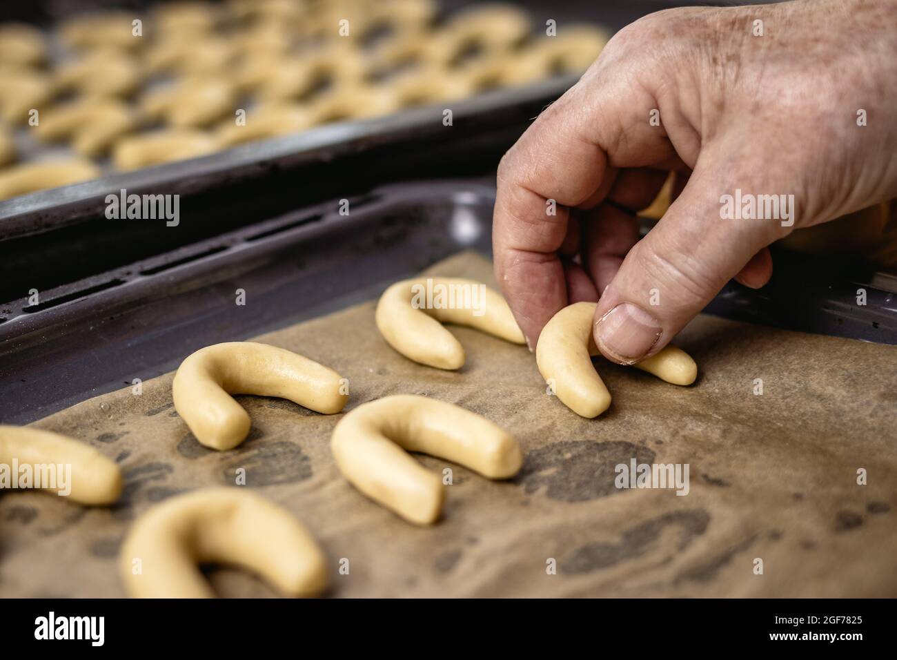 Donna anziana sta mettendo i rotoli della mezzaluna della vaniglia sa come vanillekipferl sul vassoio di cottura i dolci di natale fatti in casa pronti per la cottura Foto Stock