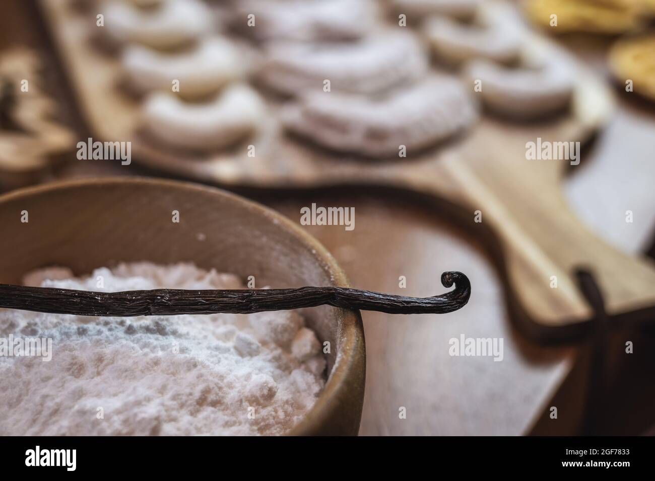Cottura con cialda di vaniglia o fagiolo. Ciotola di legno con zucchero e vanillekipferl. Biscotti di Natale sul tavolo Foto Stock