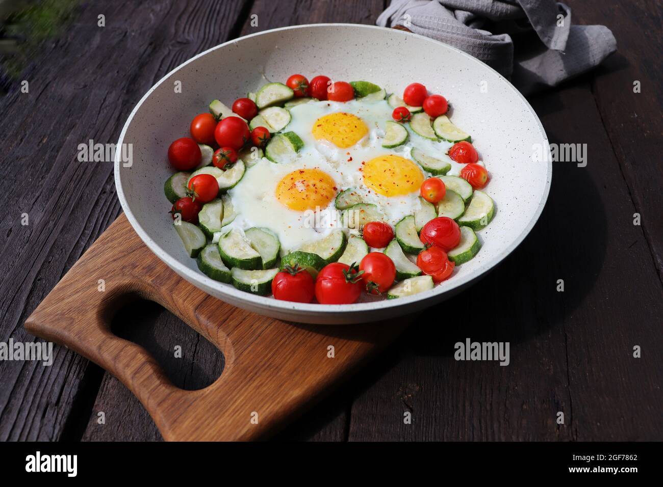 Colazione a tarda ora, uova fritte con zucchine, tomi di ciliegia. Shakshuka in padella su sfondo rustico. Cucina araba. Cibo Kosher. Foto Stock