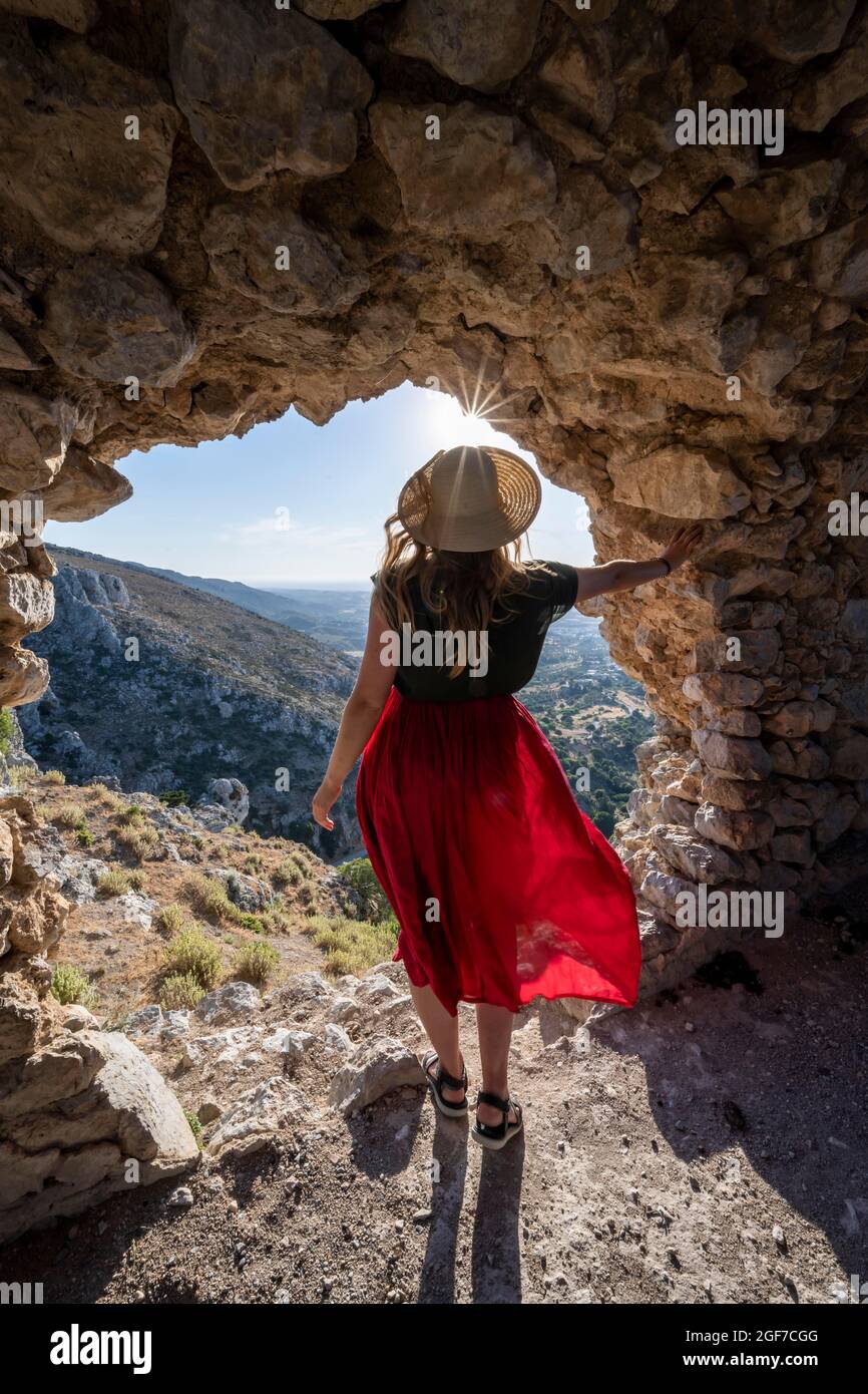 Giovane donna che guarda attraverso il foro nel muro del castello, rovine del castello di Paleo Pyli, tramonto, os, Dodecaneso, Grecia Foto Stock
