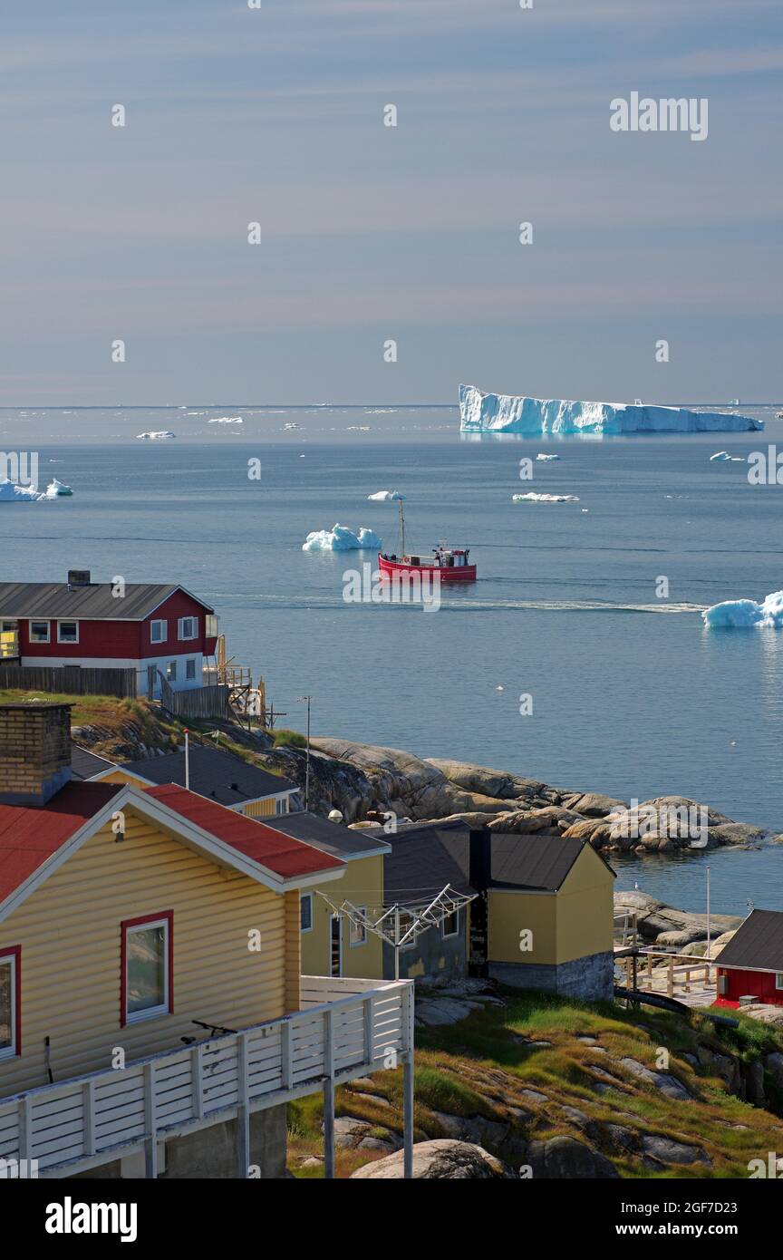 Case di legno di fronte ad una baia con barche da pesca e iceberg, Artico, Disko Bay, Ilulissat, Groenlandia, Danimarca Foto Stock