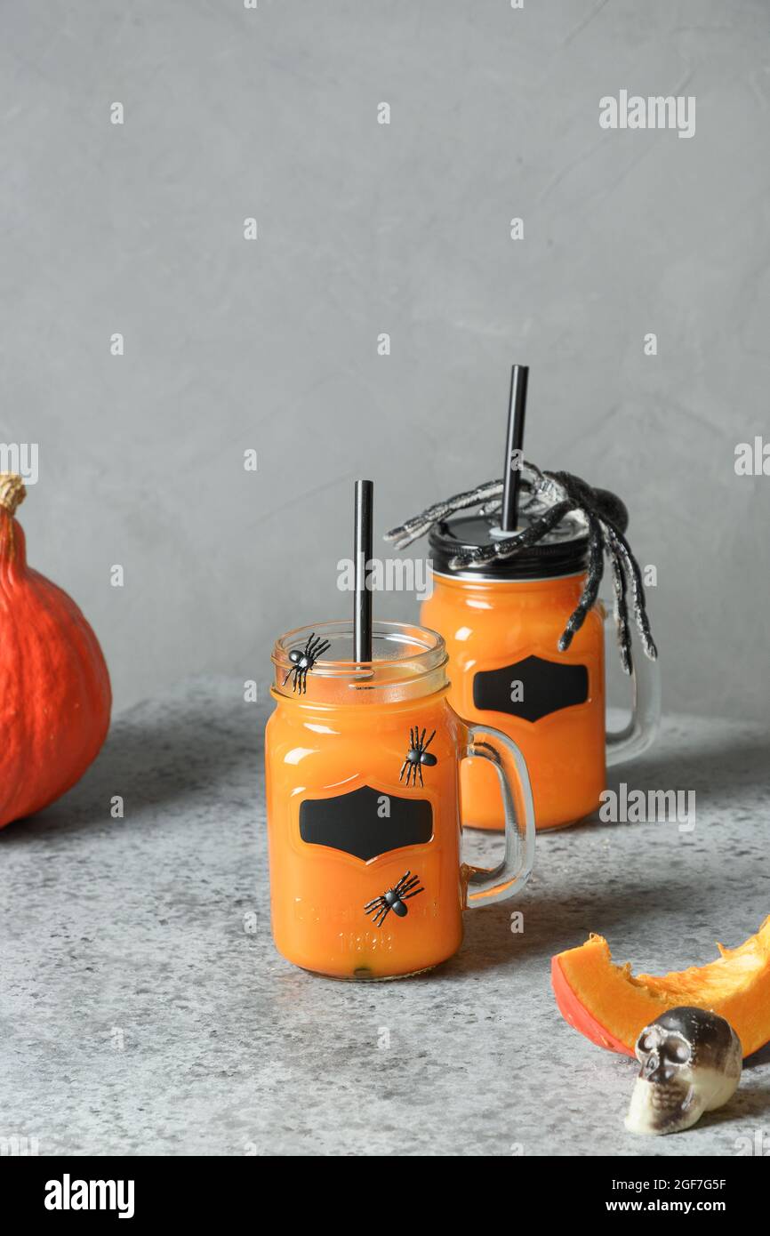 I cocktail di zucca di Halloween guarnono ragni per feste su sfondo grigio con horror cobbweb. Formato verticale. Foto Stock