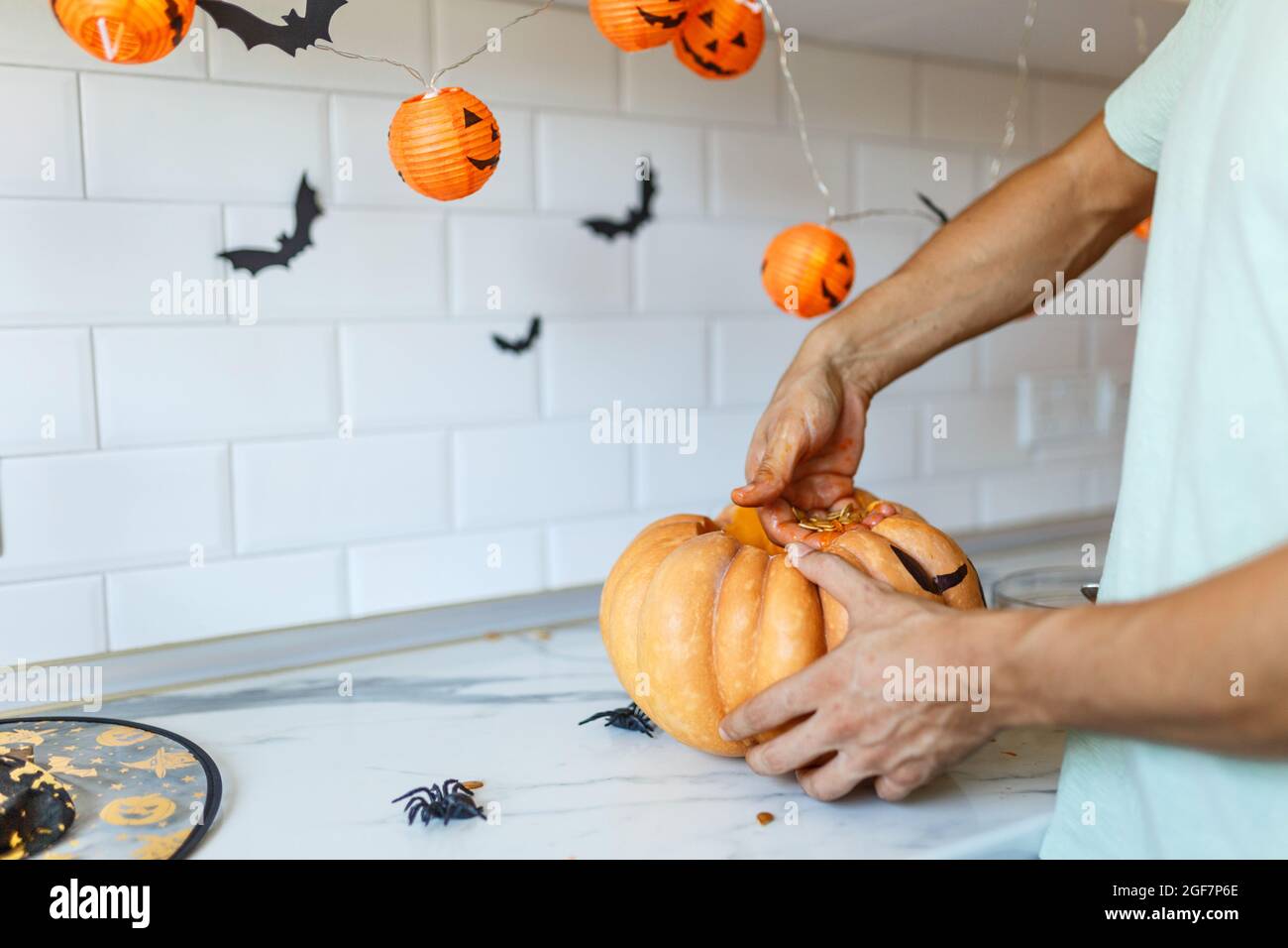 Un primo piano della mano dell'uomo tira semi e materiale fibroso da una zucca prima di intagliare per Halloween. Jack-o-lanterna. Vista laterale in cucina. Foto Stock