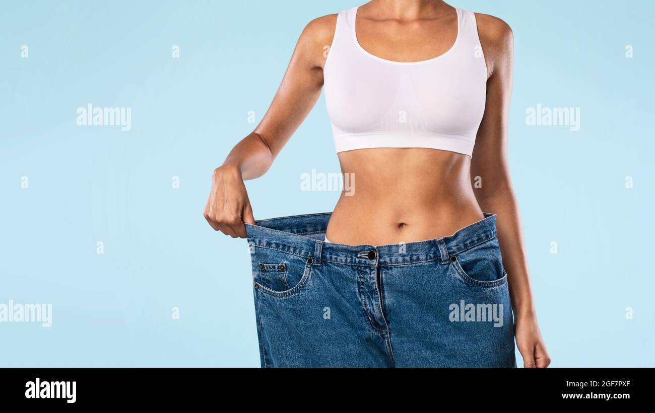 Primo piano di Donna tirando i suoi vecchi jeans larghi sciolti Foto Stock