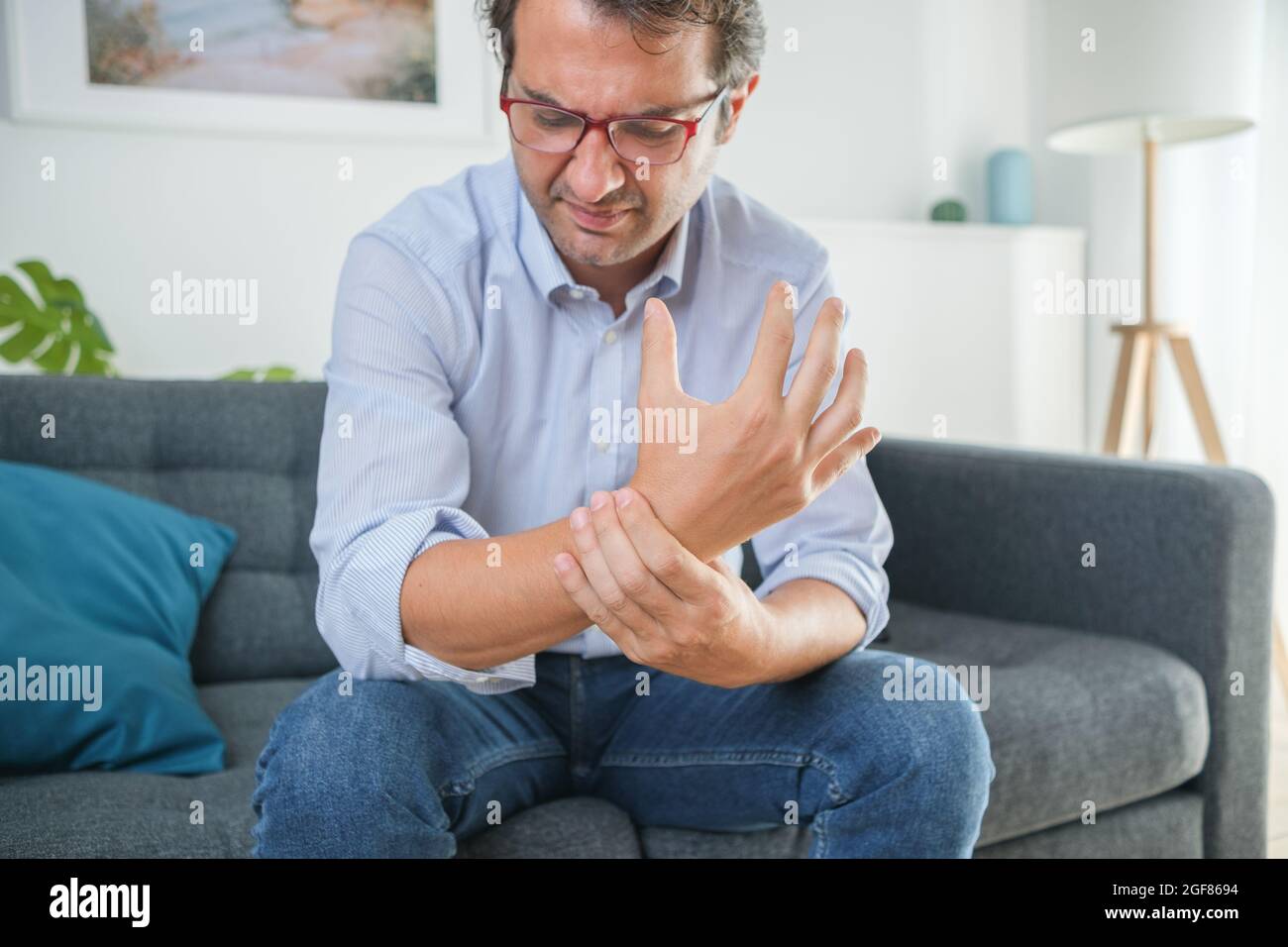 Uomo sofferente di dolore al polso seduto sul divano Foto stock - Alamy