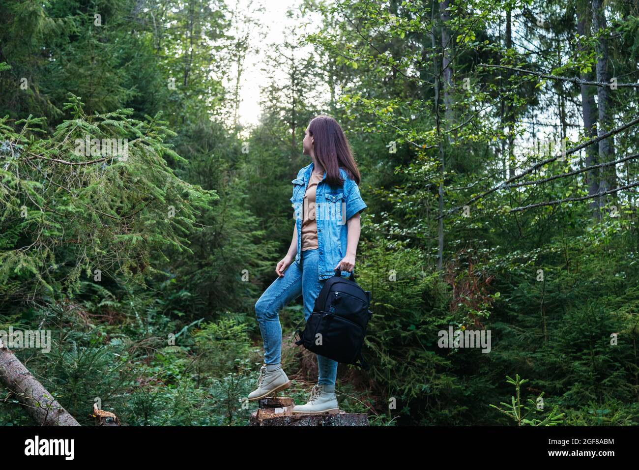 Donna in denim vestito in stivali con Photo zaino è impegnato in escursioni nella foresta. Giovane caucasica irriconoscibile che cammina nella natura nel parco Foto Stock