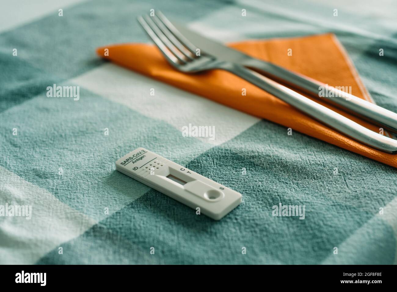 primo piano di un dispositivo di test diagnostico dell'antigene covid-19 su un tavolo per il pranzo, accanto ad un tovagliolo di tessuto arancione, una forchetta e un coltello Foto Stock