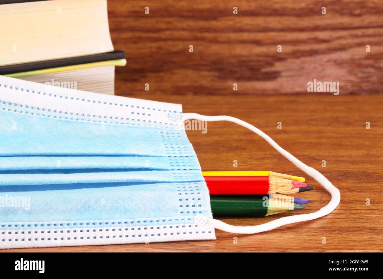 Libri, matite colorate e maschera medica simboleggiano le regole di protezione richieste per il ritorno a scuola e le istituzioni di apprendimento durante la pandemia di coronavirus Foto Stock