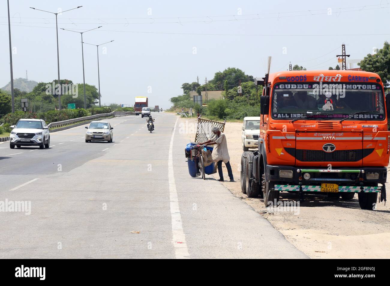 Beawar, Rajasthan, India, 24 agosto 2021: L'uomo povero indiano trasporta le merci sulla sua bicicletta mentre molti veicoli passano sulla Ahmedabad-Delhi National Highway in Beawar. Credit: Sumit Saraswat/Alamy Live News Foto Stock