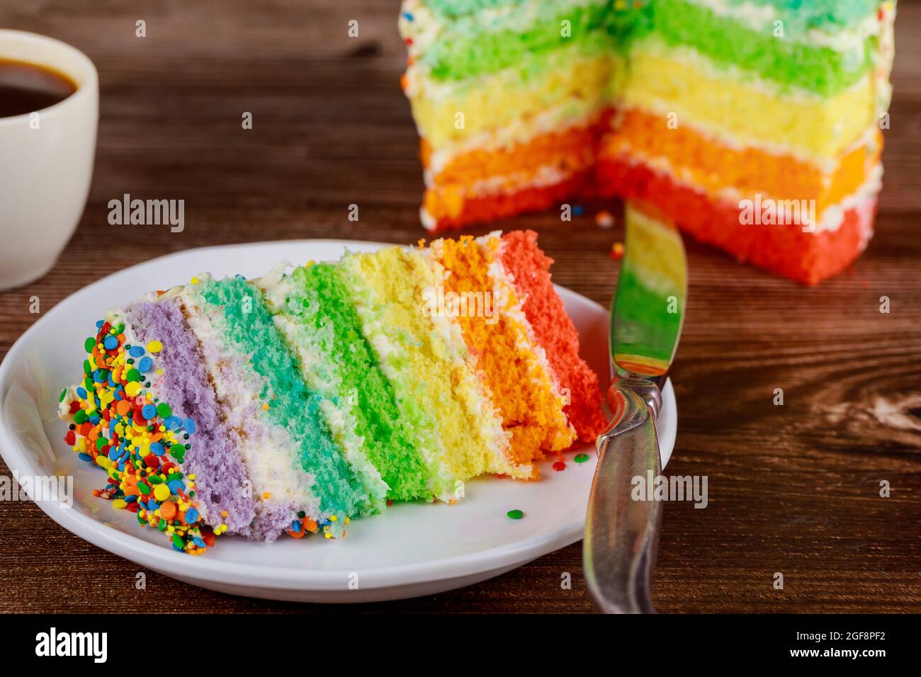Torta di compleanno colorata arcobaleno con tazza di caffè e coltello. Foto Stock