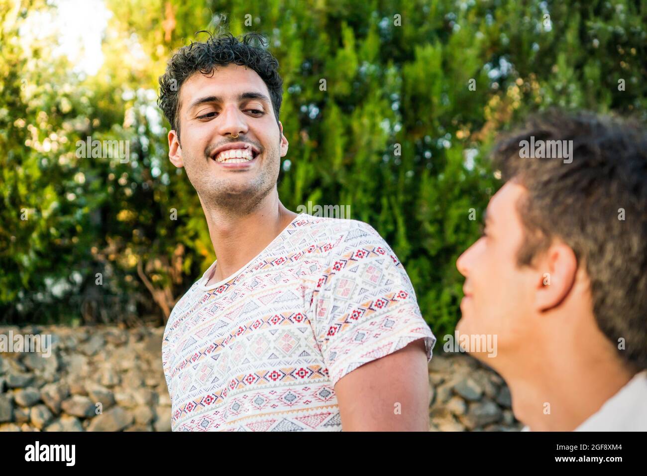 Una coppia gay che si prende una passeggiata nei sobborghi mentre si ha una bella chiacchierata. Due ragazzi sorridenti che si divertono a chiacchierare in una soleggiata giornata estiva. Una data romantica su vacat Foto Stock