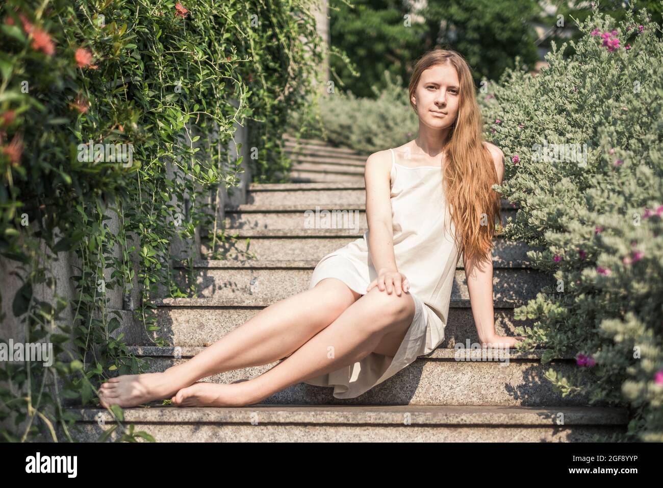 Bella giovane donna caucasica in abito bianco seduto sulle scale nel parco. Capelli biondi lunghi. Foto di alta qualità Foto Stock