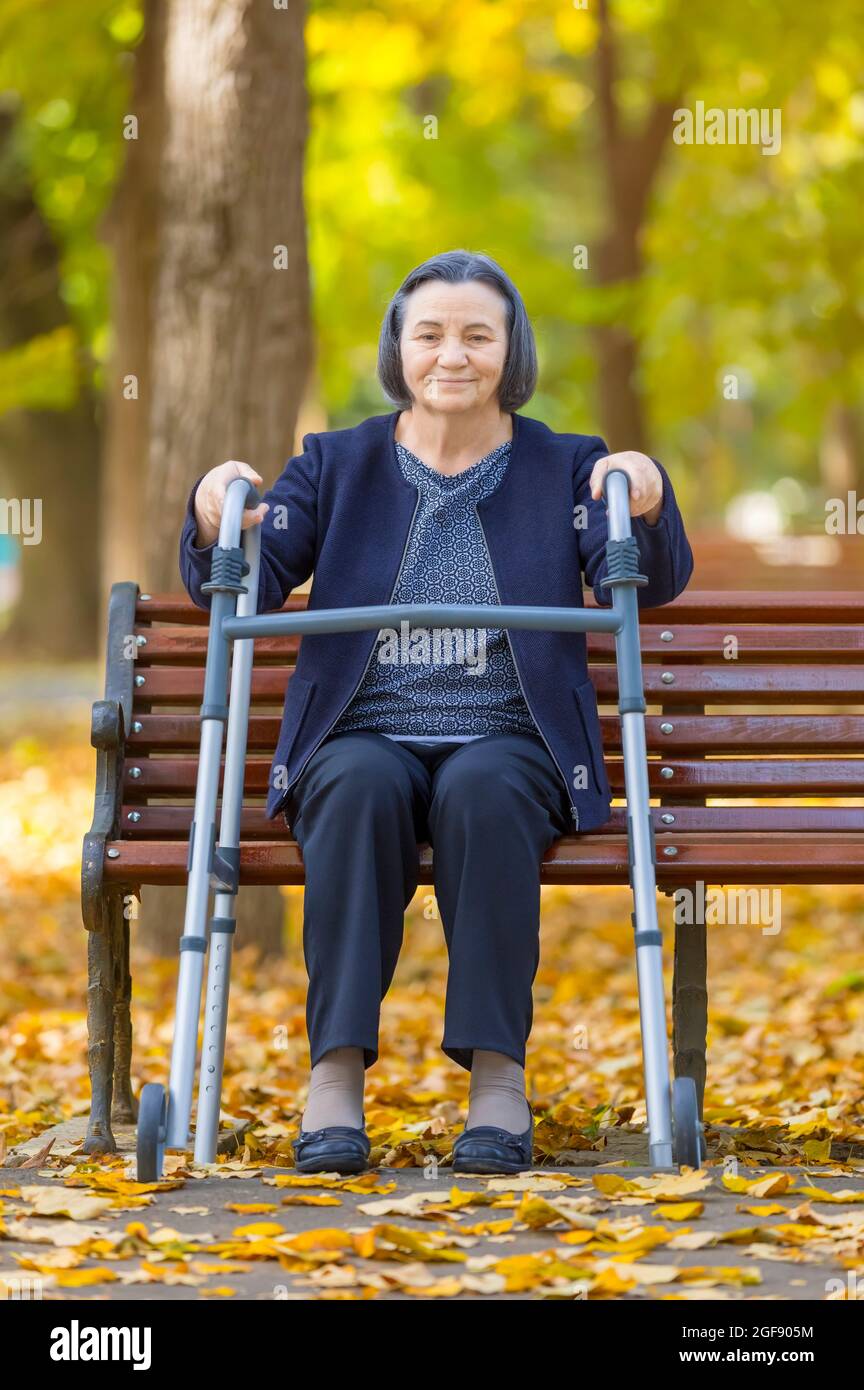 Donna con camminatore seduto su panchina nel parco autunnale Foto Stock