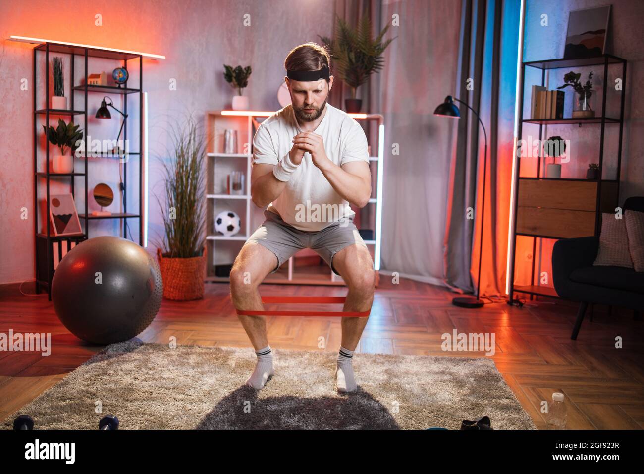 Uomo di mezza età concentrato in abbigliamento casual, fascia e calzini utilizzando la fascia resistente per l'allenamento a casa. Concetto di persone, fitness e attività domestica. Foto Stock