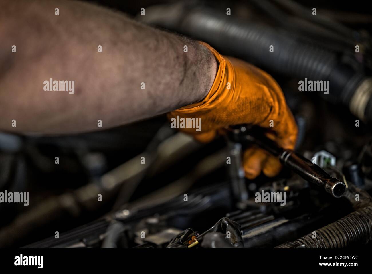 Un uomo che indossa un guanto arancione che fissa e che fa manutenzione su un motore auto in un negozio di riparazione auto Foto Stock