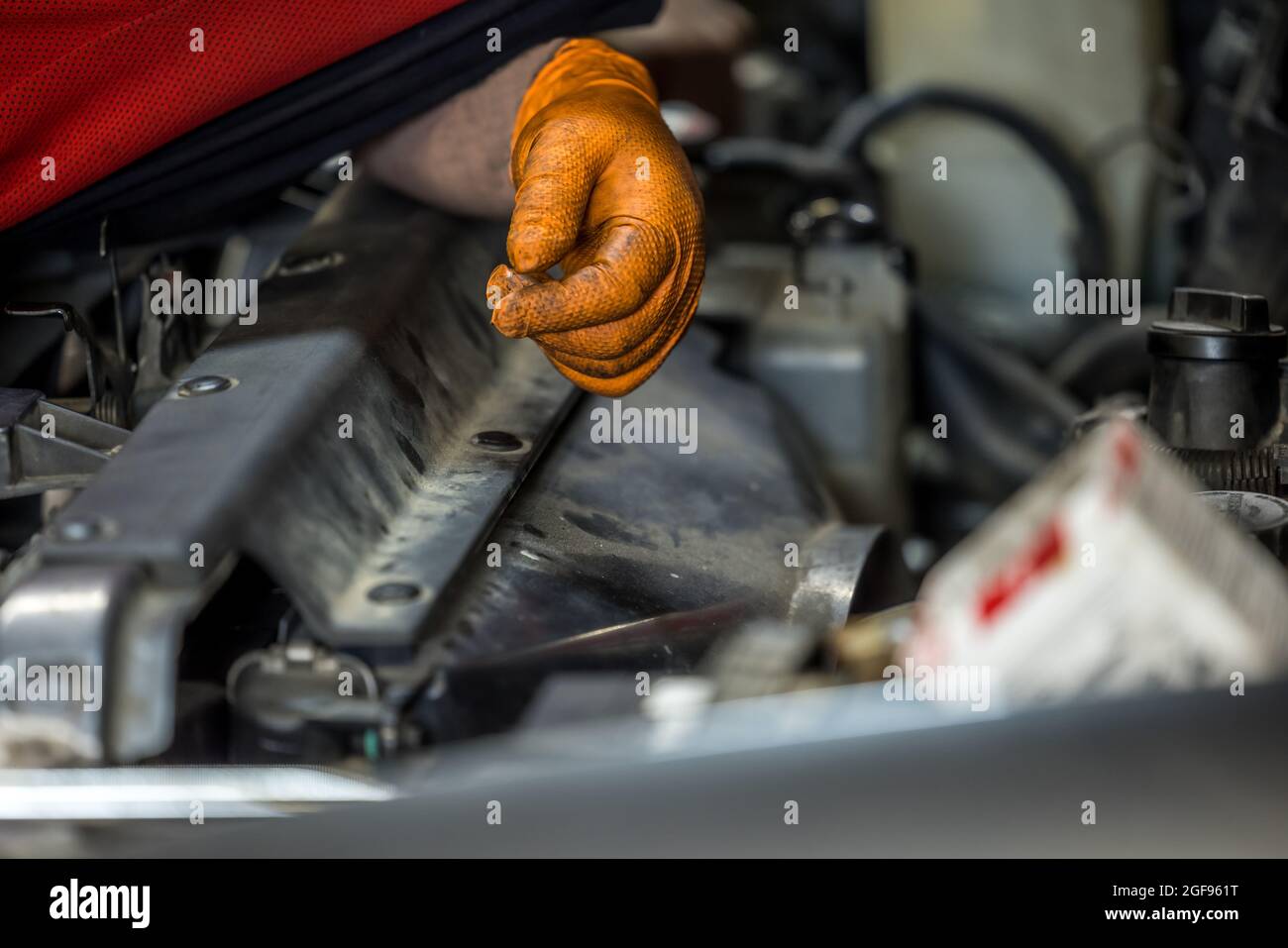Un uomo che indossa un guanto arancione che fissa e che fa manutenzione su un motore auto in un negozio di riparazione auto Foto Stock