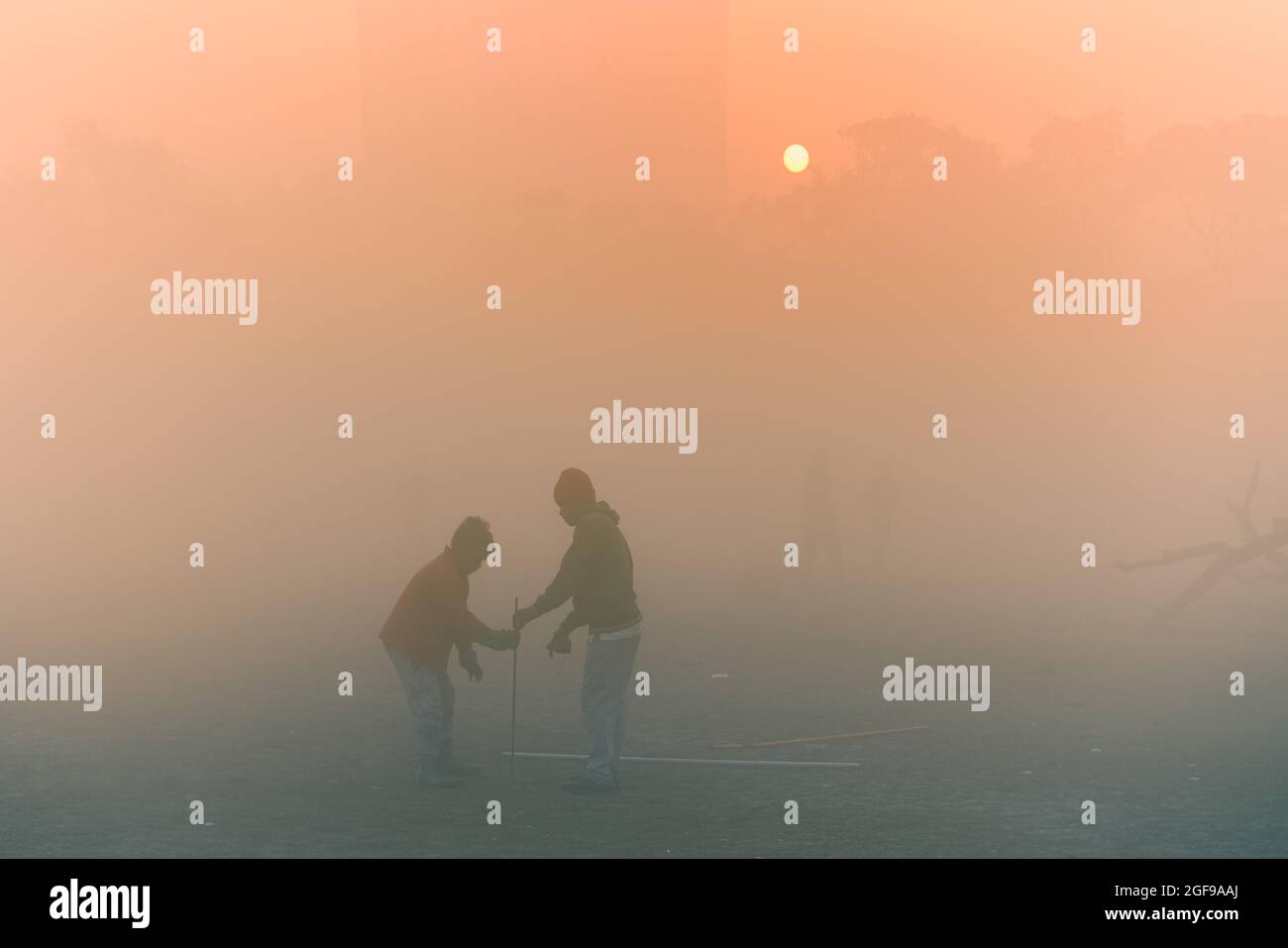 Bella immagine dell'alba a Kolkata Maidan in una mattinata d'inverno nebbia. L'alba all'orizzonte con due giovani ragazzi che mettono su il wicket per giocare il cricket. Foto Stock