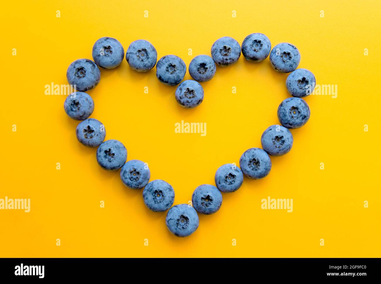 Simbolo del cuore a base di mirtilli su sfondo giallo. Concetto di salute del cuore. Foto Stock