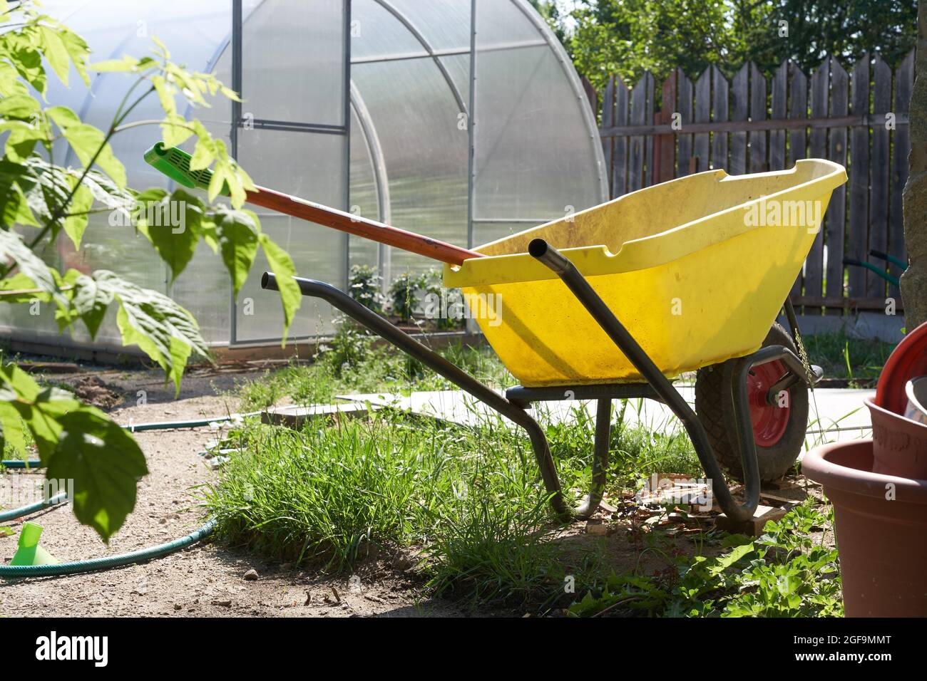 Primo piano di una moderna serra in policarbonato. Attrezzi agricoli e un carrello con una ruota in giardino. Il concetto di giardinaggio moderno. Foto di alta qualità Foto Stock