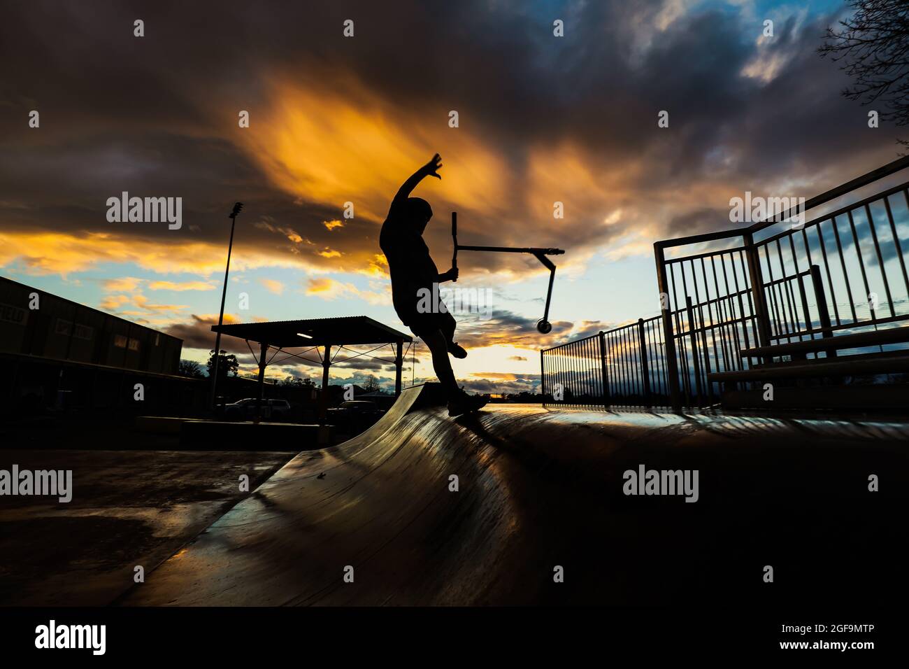 Silhouette di un ragazzo che guida uno scooter kick in un parco pattini durante il tramonto Foto Stock