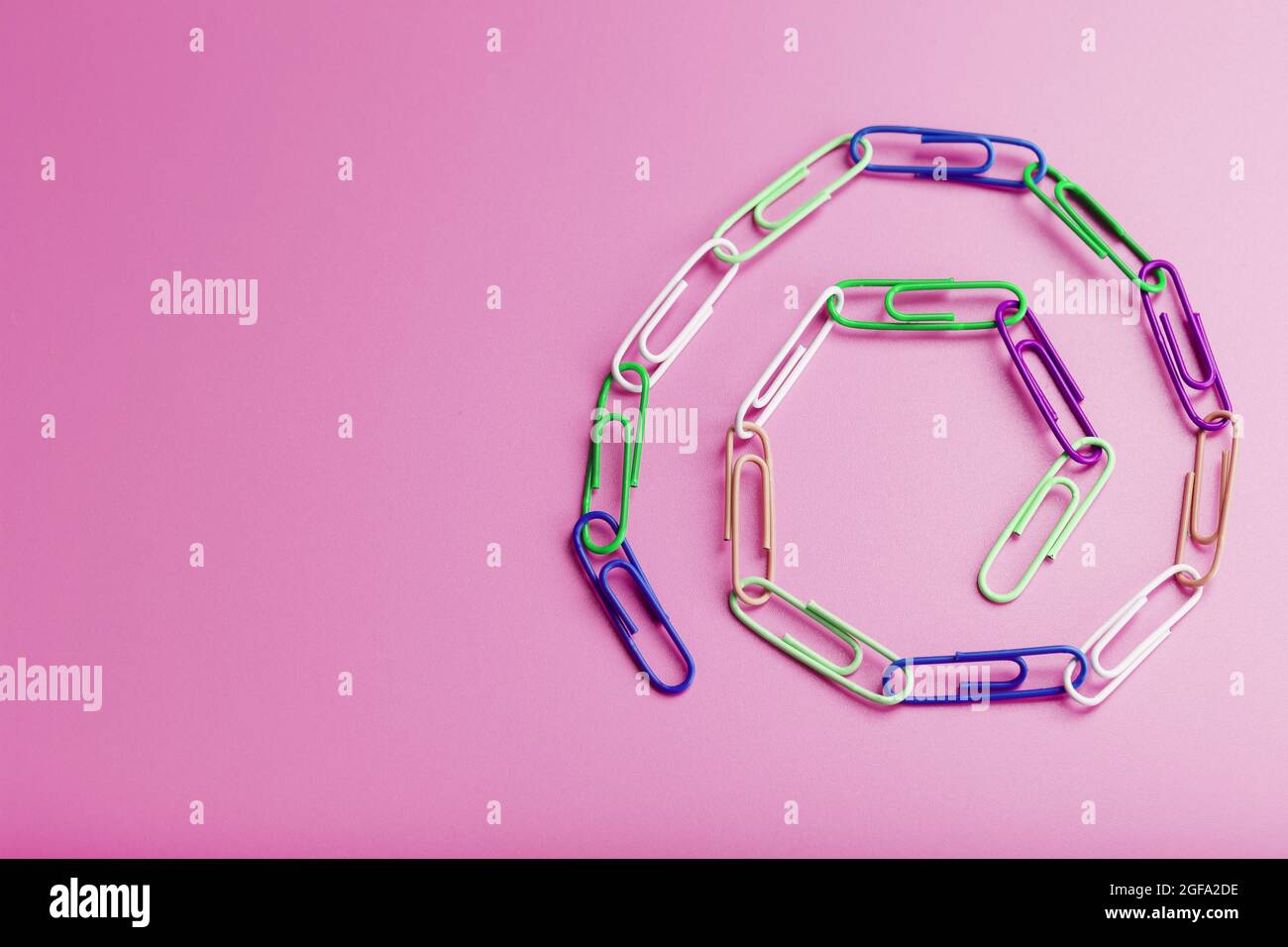 Una catena di graffette in carta multicolore su sfondo rosa. Concetto di comunicazione e cooperazione commerciale Foto Stock