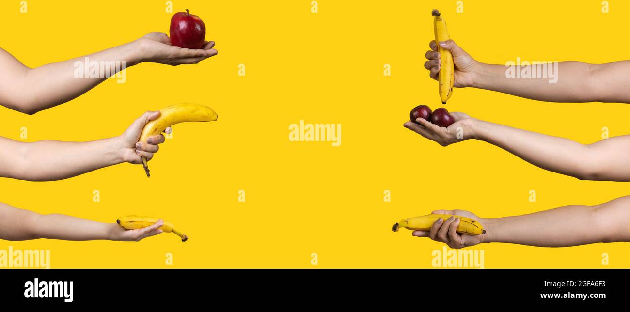 Mani con mela matura, banana e prugne isolate su sfondo giallo Foto Stock