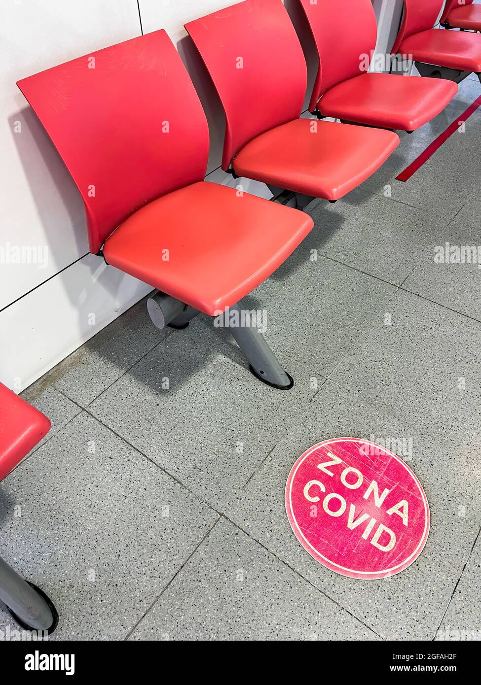 Sala d'attesa dell'ospedale con sedie rosse e un cartello rosso sul pavimento con il testo (zona COVID) che contrassegna l'area per i pazienti affetti da virus corona, verticale Foto Stock