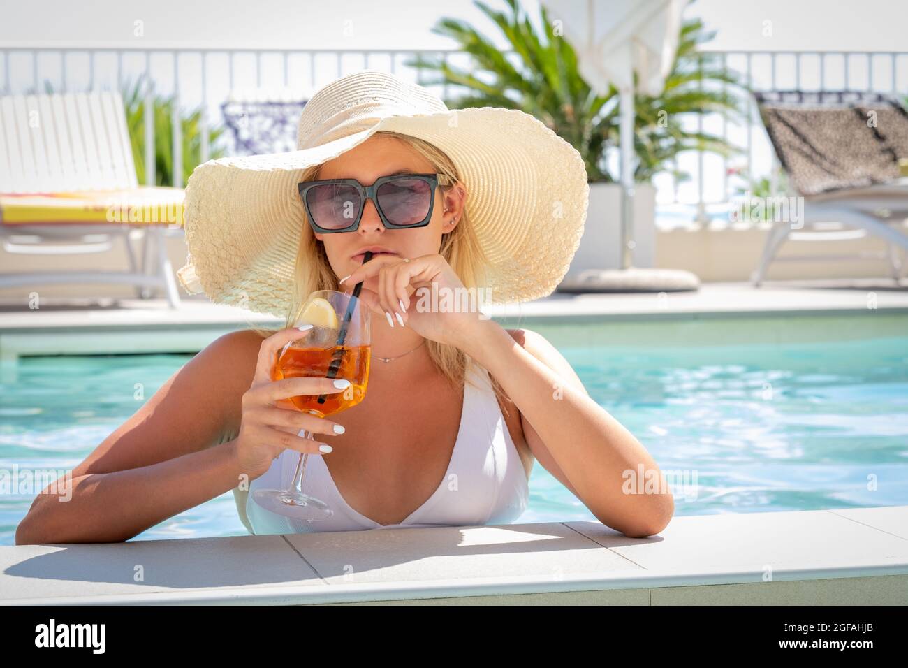 Ritratto di donna con occhiali da sole e grande cappello che beve cocktail  in piscina - bella ragazza adolescente che ha una rinfrescante bevanda  analcolica loo Foto stock - Alamy