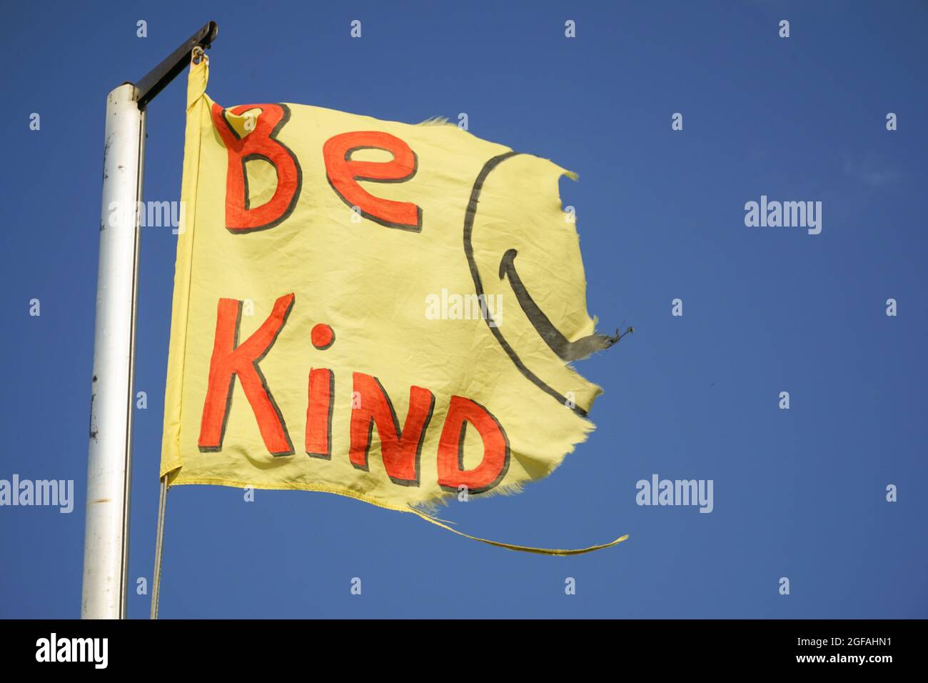 East Wittering, UK, 23 agosto 2021: Una bandiera gialla adornata dal messaggio 'essere gentile' e i resti di una faccia sorridente vola sullo sfondo o Foto Stock