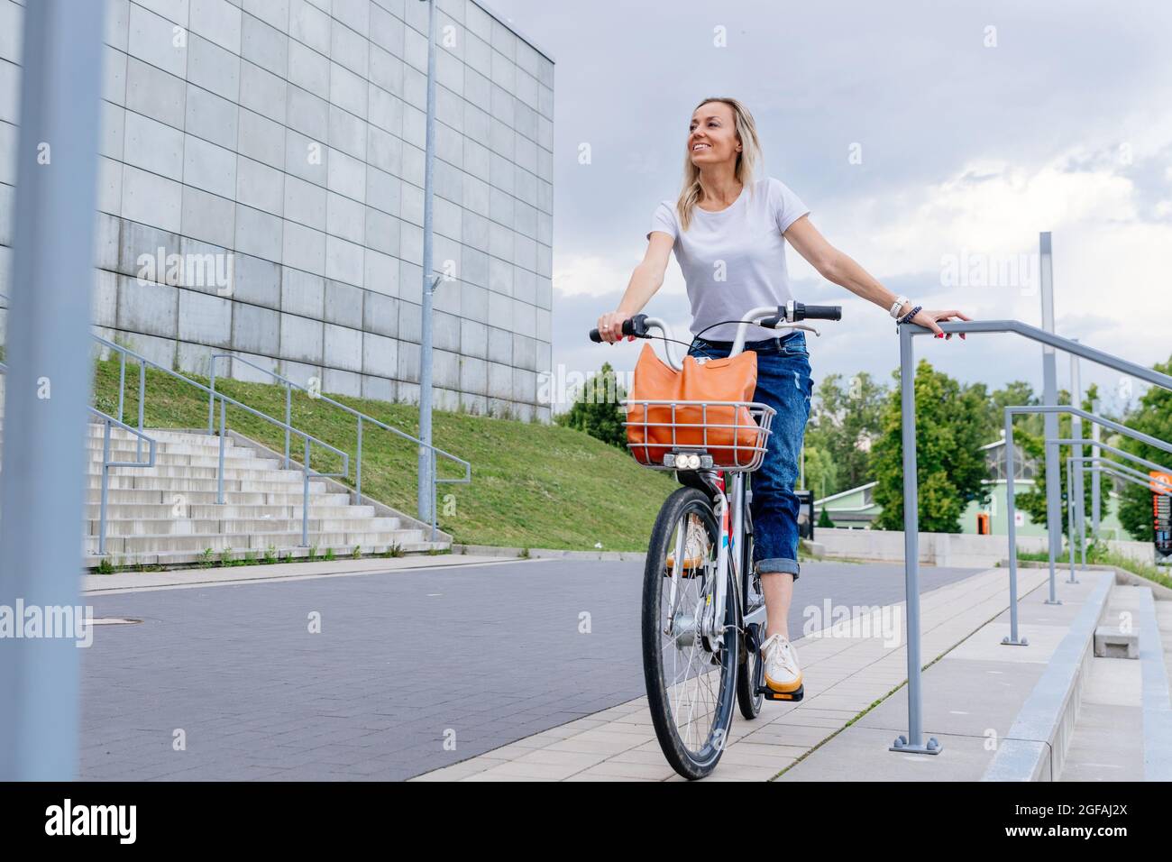 Bella e allegra donna godere di giro in bicicletta nella soleggiata città attività di svago all'aperto. Foto Stock
