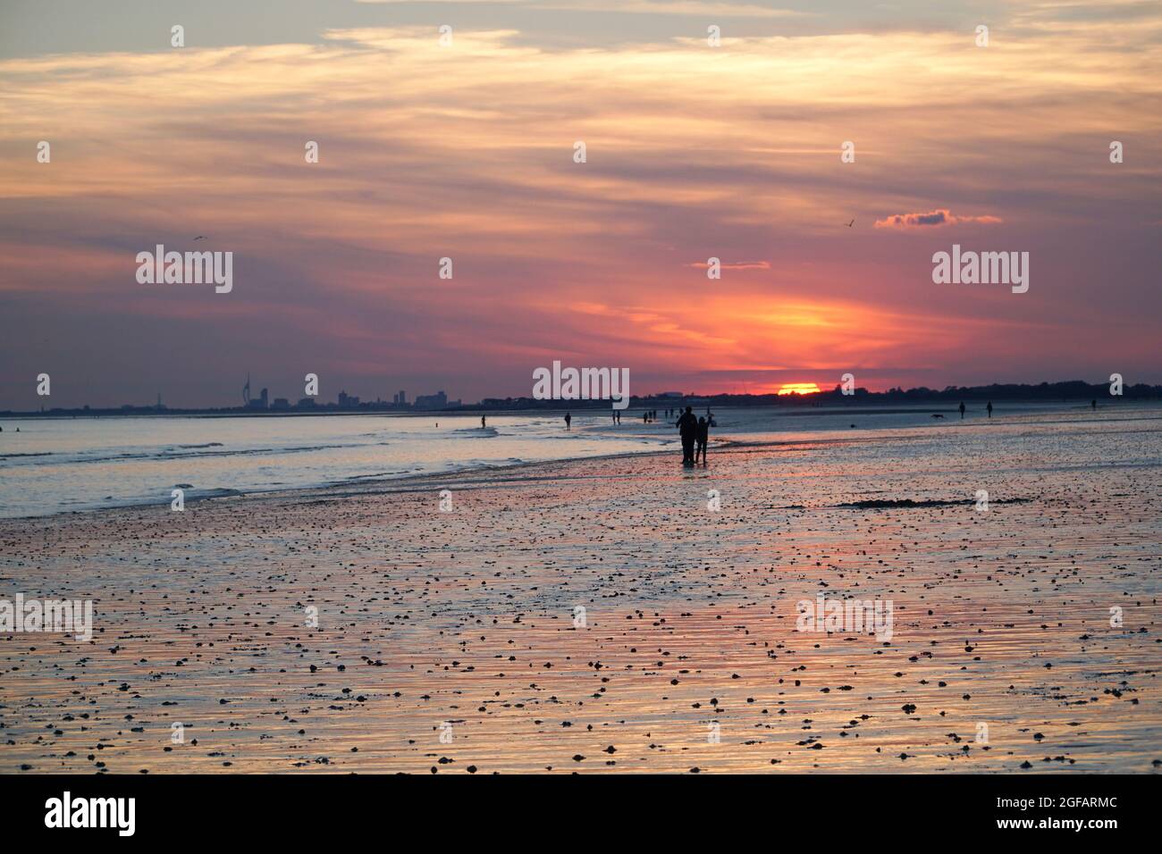East Wittering, UK, 23 agosto 2021: Persone e cani godersi il tempo secco sulla spiaggia di East Wittering nel Sussex occidentale mentre il sole tramonta sul Solen Foto Stock