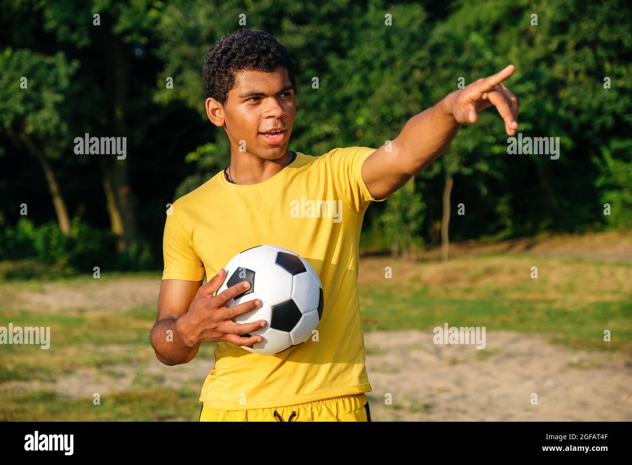 Giovane uomo brasiliano sorridente tiene una palla prima di giocare su una spiaggia di sabbia erbosa Foto Stock