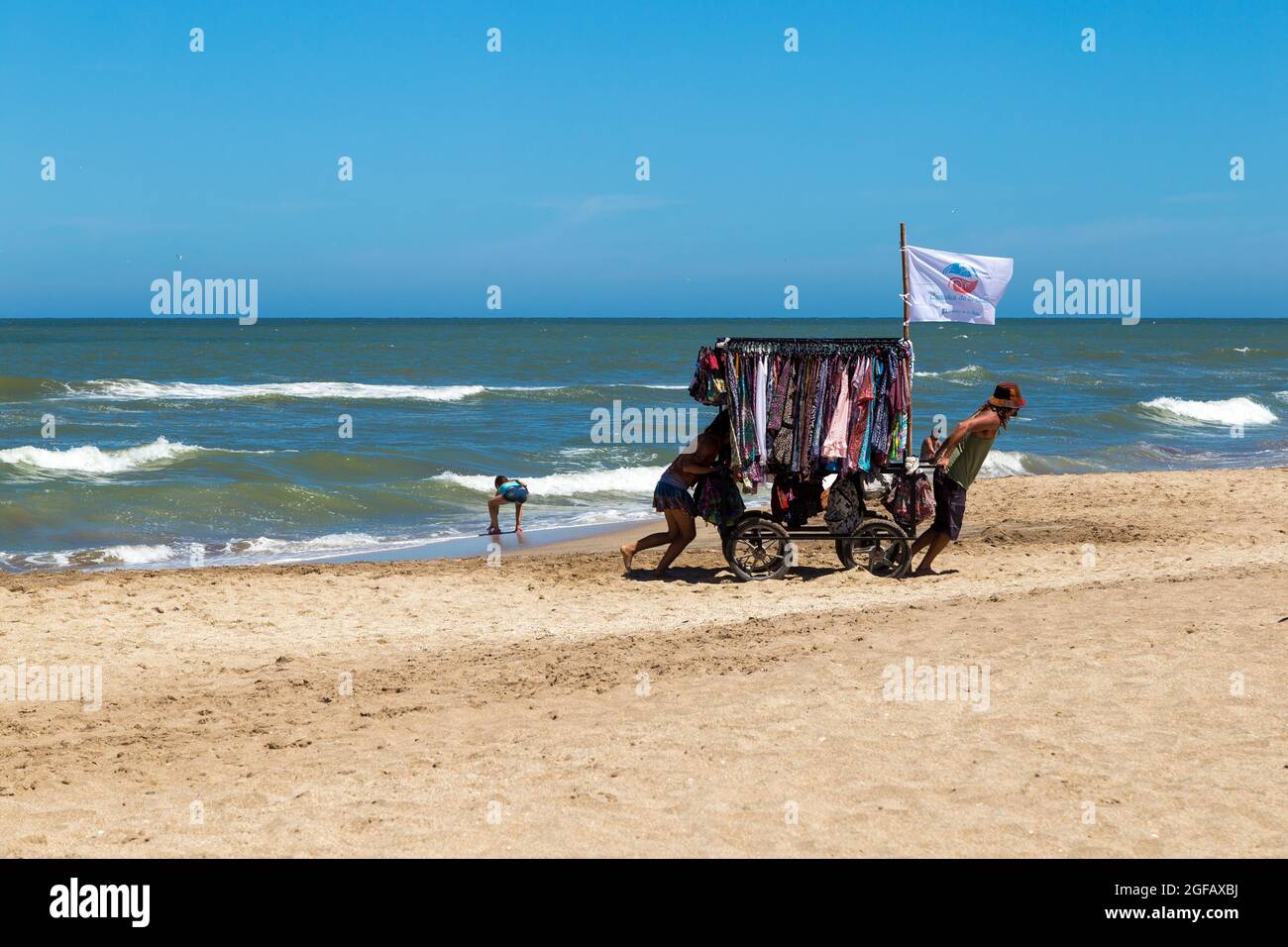 Un paio di peddlers che spostano i loro vestiti si stalla sulla spiaggia in una giornata di sole della stagione estiva. Foto Stock