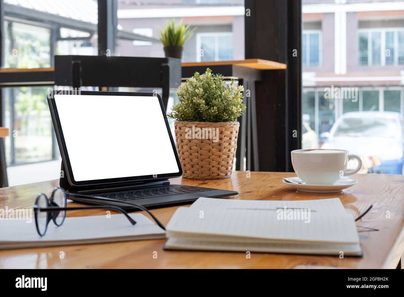 Un tablet digitale con schermo bianco vuoto, tastiera, tazza di caffè sulla scrivania Foto Stock