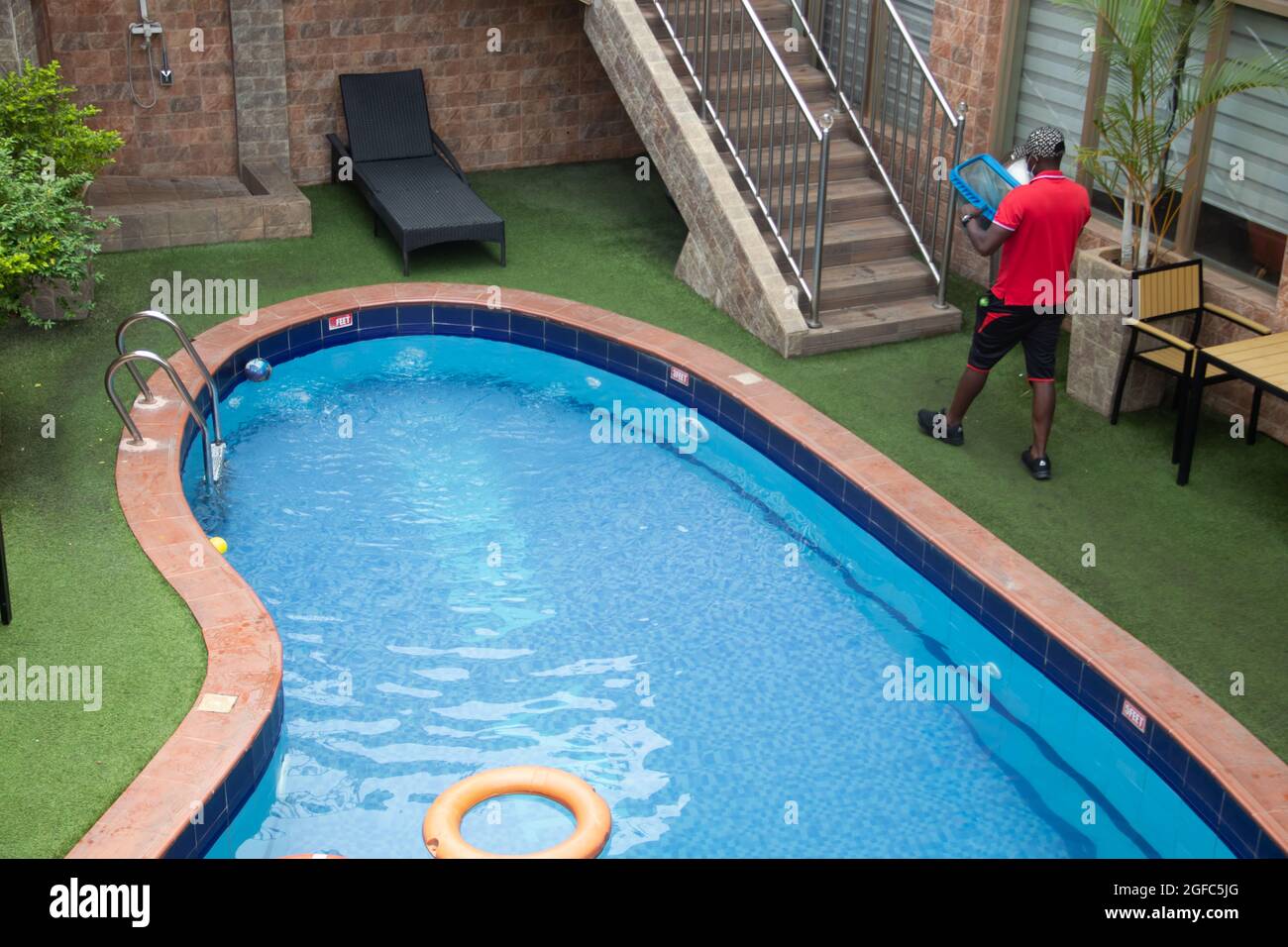 Pulizia della piscina da pool-guy, utilizzando la rete. Piante decorative accanto alla piscina Foto Stock