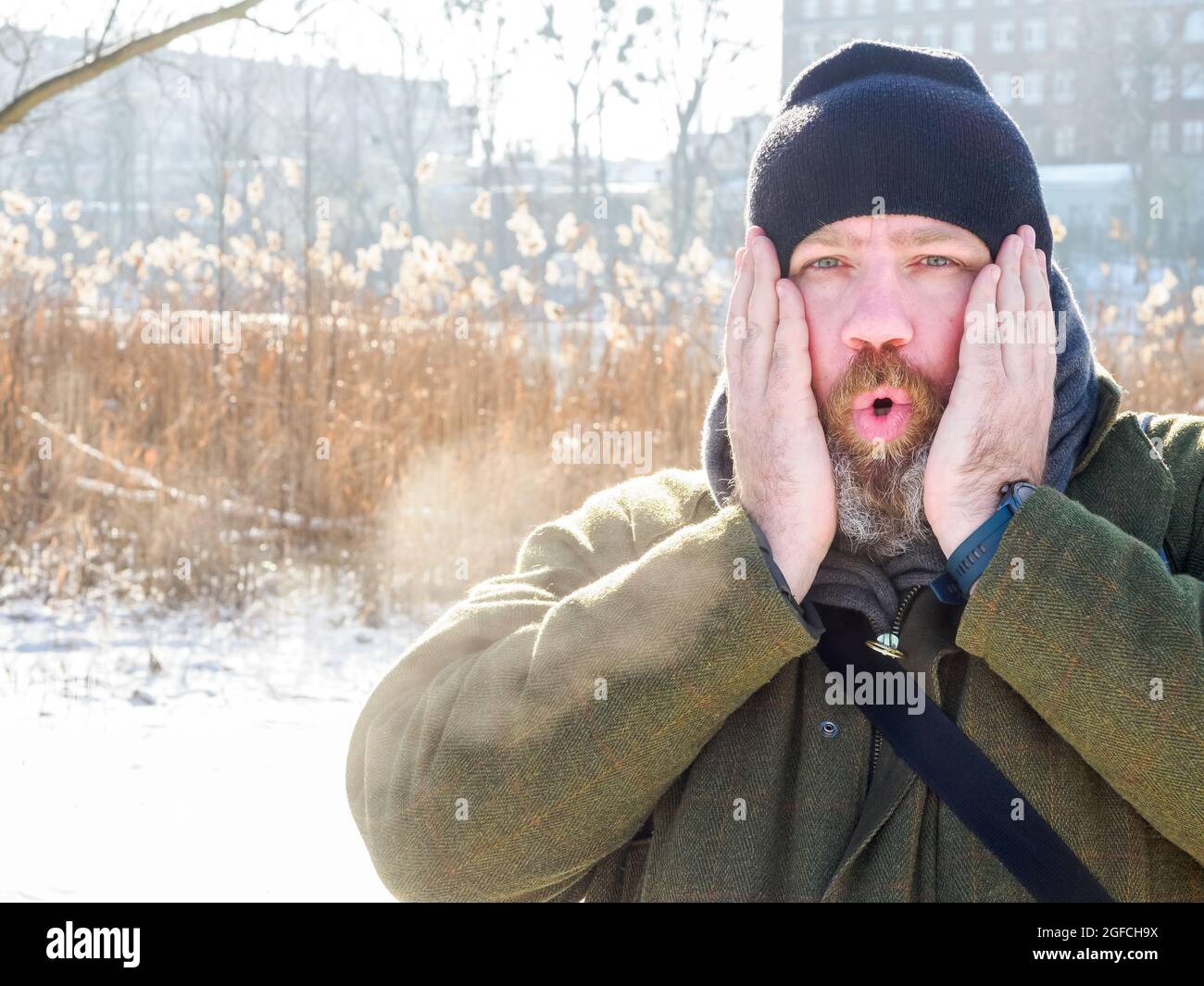 L'uomo respira nella foresta d'inverno. Uomo adulto che indossa un cappello a maglia, metti le mani sul viso e respira aria fredda. Uomo bearded che si rilassa sulla passeggiata invernale in nevoso Foto Stock