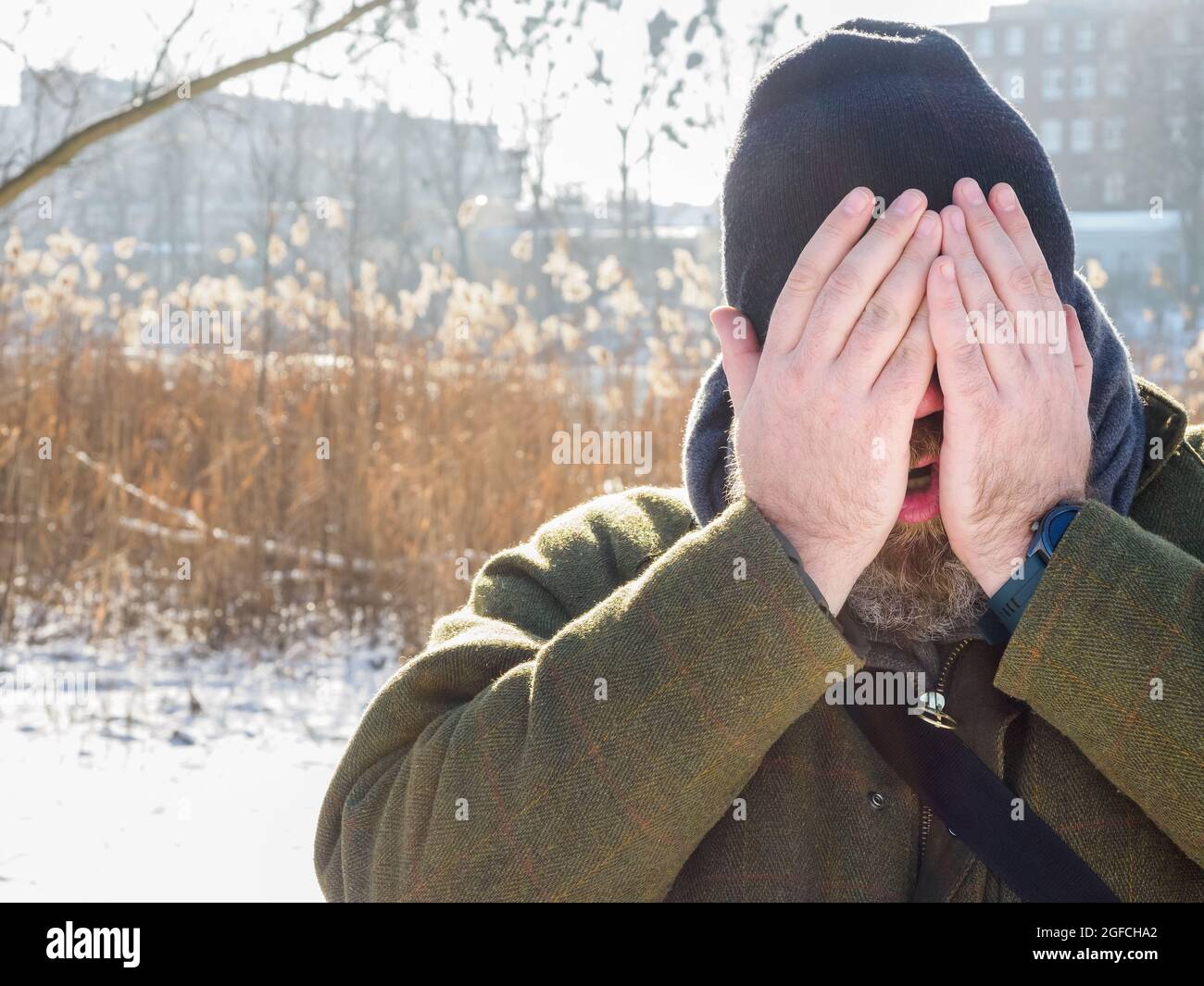 L'uomo respira nella foresta d'inverno. Uomo adulto che indossa il cappello a maglia, chiude il viso con le mani respirando aria fredda. Uomo bearded sulla passeggiata di inverno in fores nevoso Foto Stock