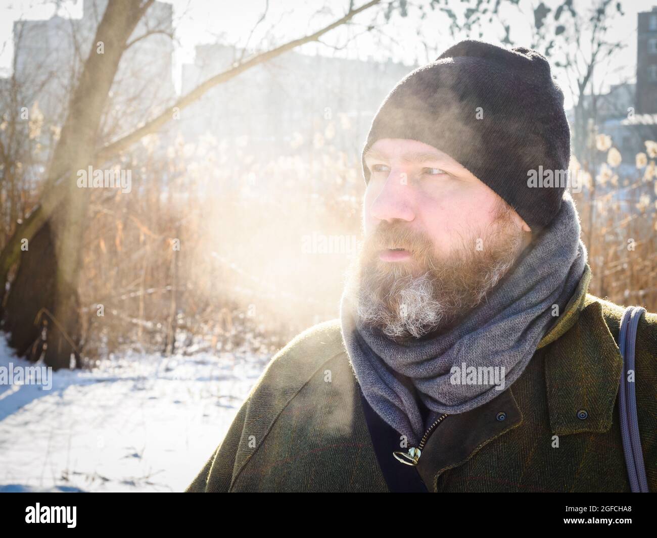 L'uomo respira nella foresta d'inverno. Uomo adulto che indossa un cappello a maglia, respirando aria fredda. Uomo bearded rilassante sulla passeggiata invernale nella foresta innevata, candid cattura, l Foto Stock