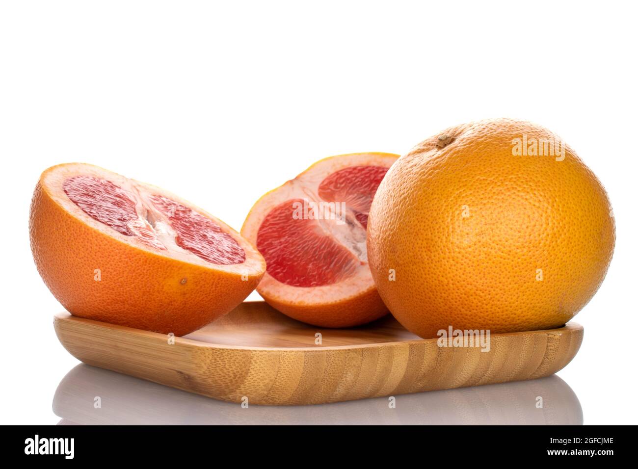 Un'intera e due metà di un delizioso pompelmo maturo su un vassoio di bambù, primo piano, isolato su bianco. Foto Stock