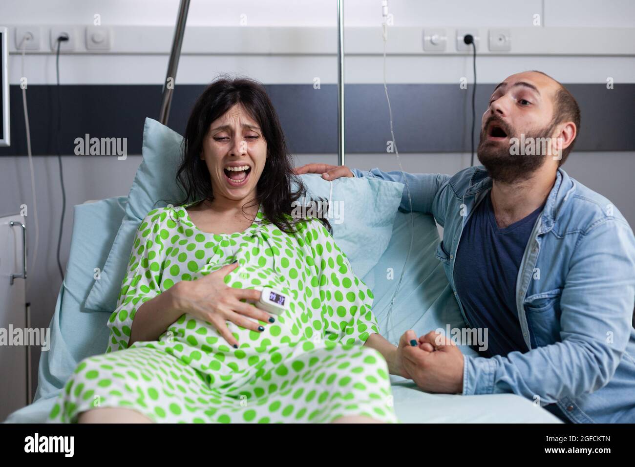 Donna incinta che entra in travaglio che ha contrazioni in ospedale reparto mentre l'uomo nervoso urla per l'infermiera e l'assistenza medica. Coppia caucasica che si prepara per il parto Foto Stock