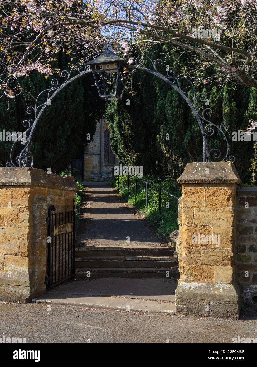 Gatempi di pietra e un arco di metallo all'ingresso della chiesa di St Mary nel villaggio di Dallington, Northampton, Regno Unito Foto Stock