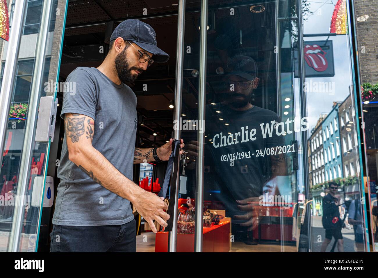 CARNABY STREET LONDRA, REGNO UNITO. 25 agosto 2021. Un assistente di negozio posiziona un nastro nero all'ingresso del negozio Rolling Stones a Carnaby Street come omaggio al batterista Rolling Stones Charlie Watts, morto all'età di 80 anni martedì. Credit amer Ghazzal/Alamy Live News Foto Stock