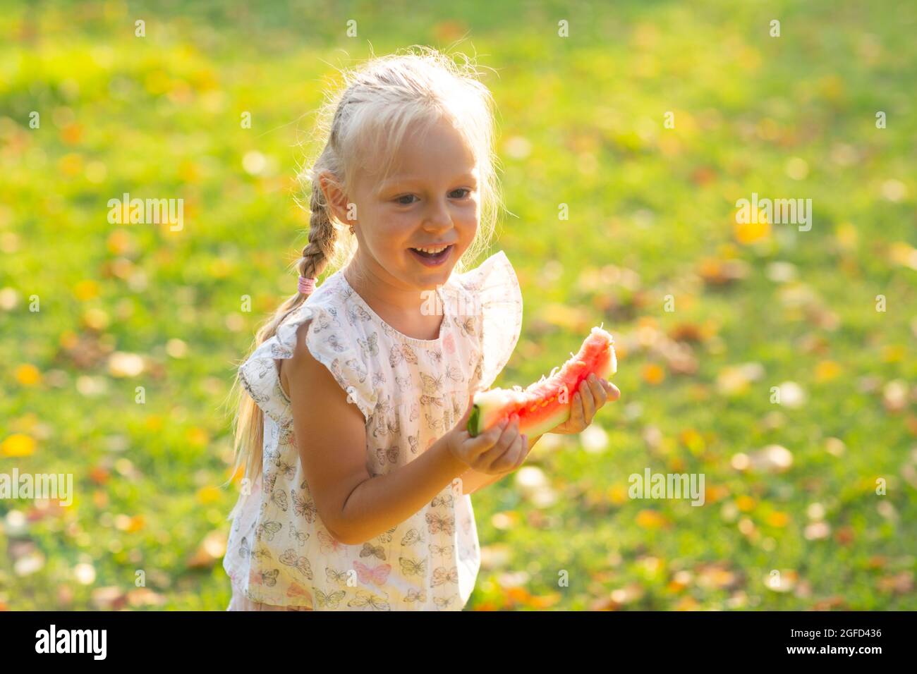 Simpatica ragazza bionda con cocomero sull'erba nel parco. Foto Stock