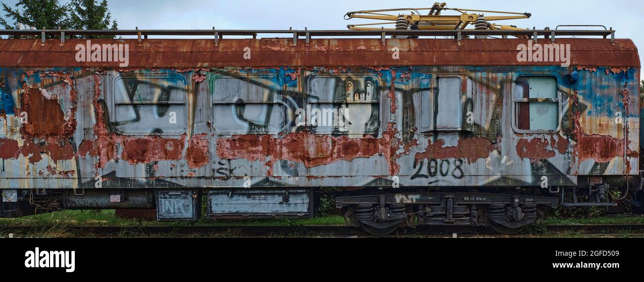 Vecchia automotrice elettrica ruggine con graffiti e pantografo, che mostra la vernice sbucciante e il degrado urbano. Foto Stock